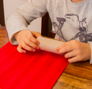 Ein Kind legt eine Toilettenpapier-Rolle auf ein rotes Papier.