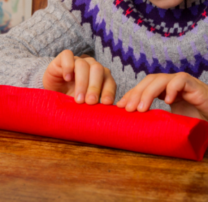 Ein Kind rollt eine Toilettenpapier-Rolle in ein rotes Papier.