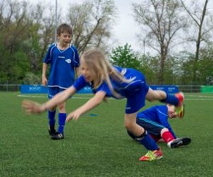 Ein Junge foult beim Fußballspielen ein Mädchen. Sie fällt hin.