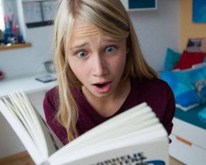 Das Mädchen Charlotte liest ein Buch. Sie reißt die Augen auf, weil sie es so spannend findet.