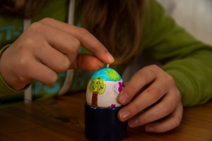 Ein Mädchen steckt ein Streichholz mit Faden in eine Eierschale.