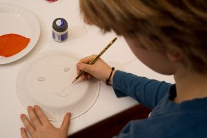 Ein Junge zeichnet ein Gesicht auf einen Teller.