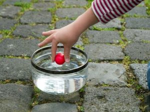 Ein Mädchen legt einen kleinen Ball aus Knete in einen Behälter voller Wasser.