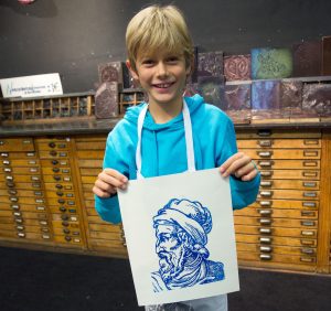 Ein Junge hält ein Papier hoch. Auf ihm ist ein blaues Bild von Johannes Gutenberg.