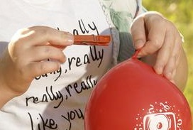 Ein Mädchen heftet eine Wäscheklammer an einen Luftballon.