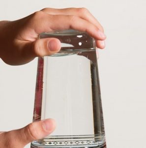 Eine Hand hält ein Glas mit Wasser falsch herum.