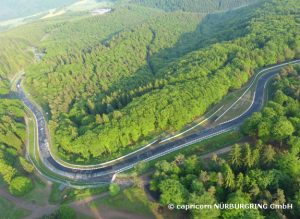 Die Rennstrecke vom Nürburgring. Man sieht einen Teil der Strecke von weit oben. Sie führt durch einen Wald.