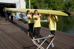Ein Ruderer-Team von Kindern und ihr Trainer tragen ein Ruderboot über einen Steg.