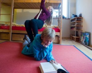 Der Junge Philipp liest ein Buch auf dem Boden. Hinter ihm springt das Mädchen Charlotte.