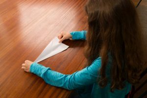 Ein Mädchen faltet eine zweite Tragfläche in einen Papierflieger.