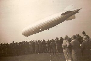 Der Zeppelin LZ 127 „Graf Zeppelin” fliegt über einer Menschenmenge. Es handelt sich um ein historisches Foto in Schwarz-Weiß.