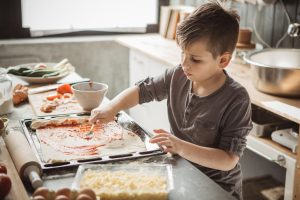 Ein kleiner Junge belegt eine Pizza in der Küche.