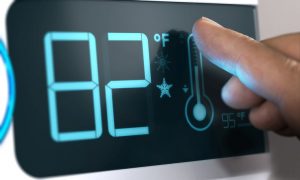 Ein Finger stellt auf einem digitalen Wärmeregler die Temperatur von 82 Grad Fahrenheit ein.