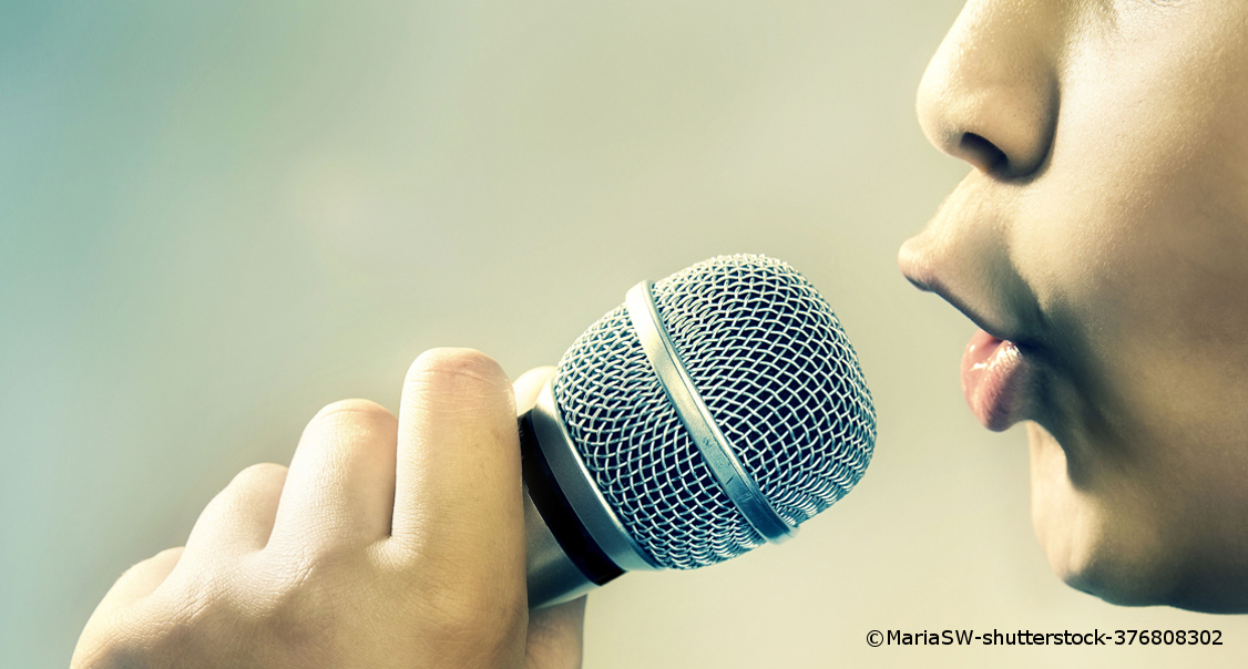 Ein Mann hält ein Mikrofon mit einer Hand an seinen Mund.