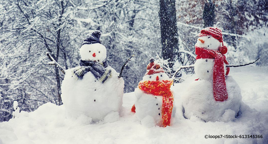 Drei Schneemänner stehen in einem Winterwald. Sie haben jeweils rote, orangene und schwarze Kleiderstücke an.