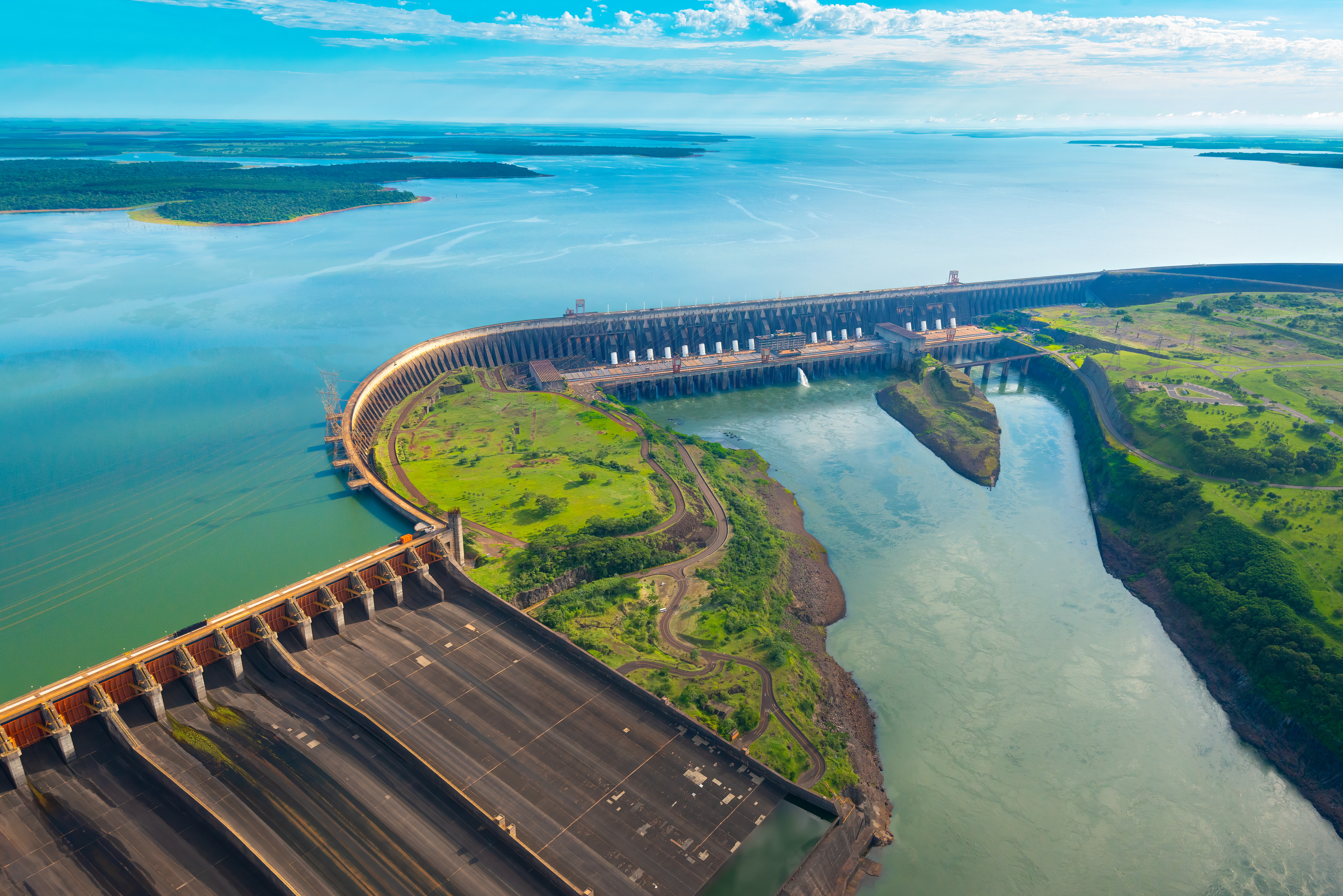 Das Itaipu Wasserkraftwerk zwischen Paraguay und Brasilien. Die Wasseroberfläche hinter dem Kraftwerk spiegelt den Himmel wieder. In östlicher Richtung fließt das Wasser des Kraftwerks wieder ab.