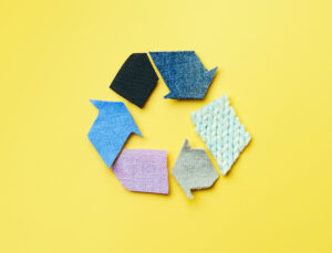 Das Symbol für "reuse, reduce, recycle" aus verschiedenfarbigen Stoffen vor einem gelben Hintergrund