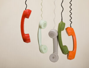 Fünf Telefonhörer in verschiedenen Farben hängen im Bild von der Decke.